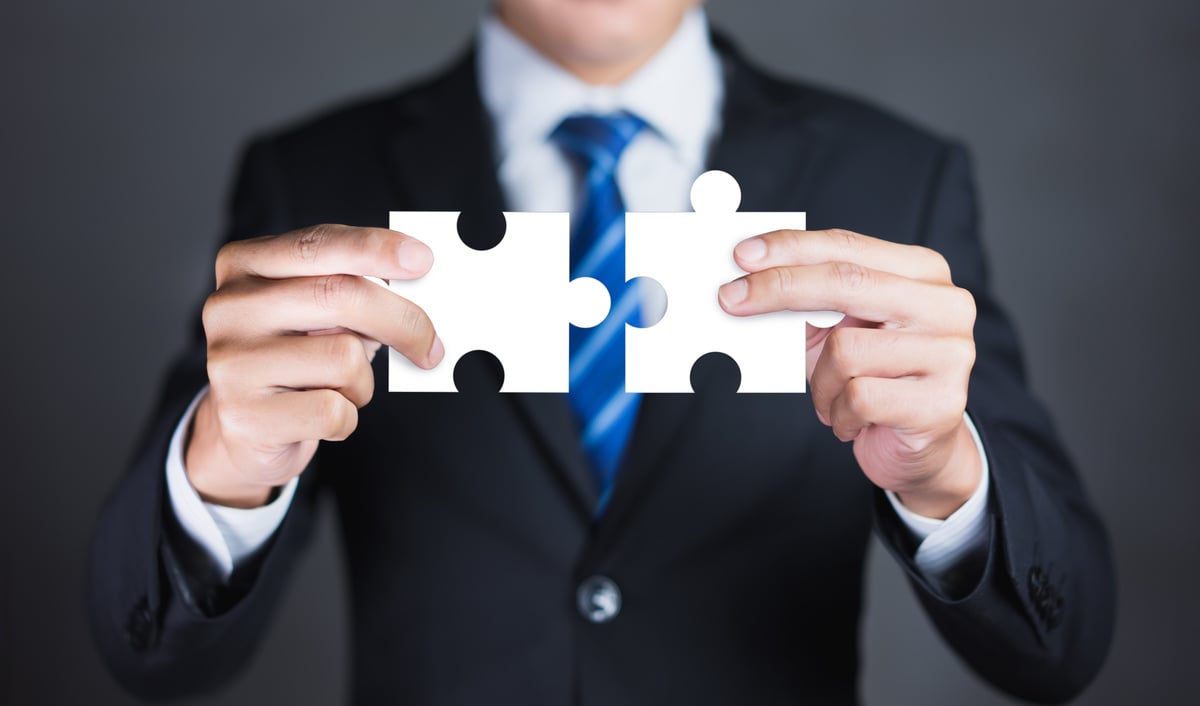 Businessman hands connecting puzzle pieces representing the merging of two companies or joint venture, partnership, Mergers and acquisition concept.